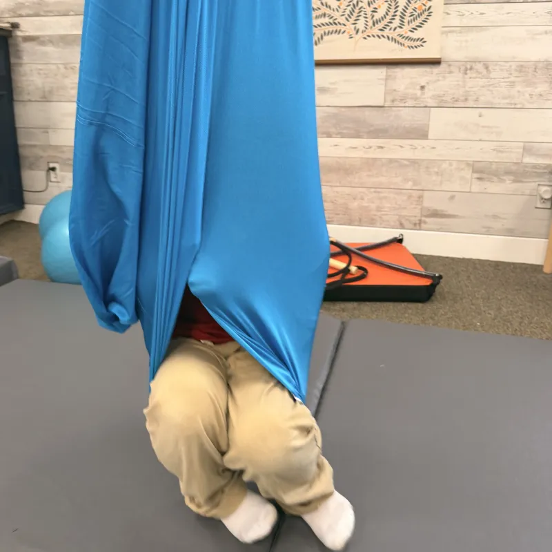 Child wrapped in a blue therapy swing cocoon in the Galveston sensory gym