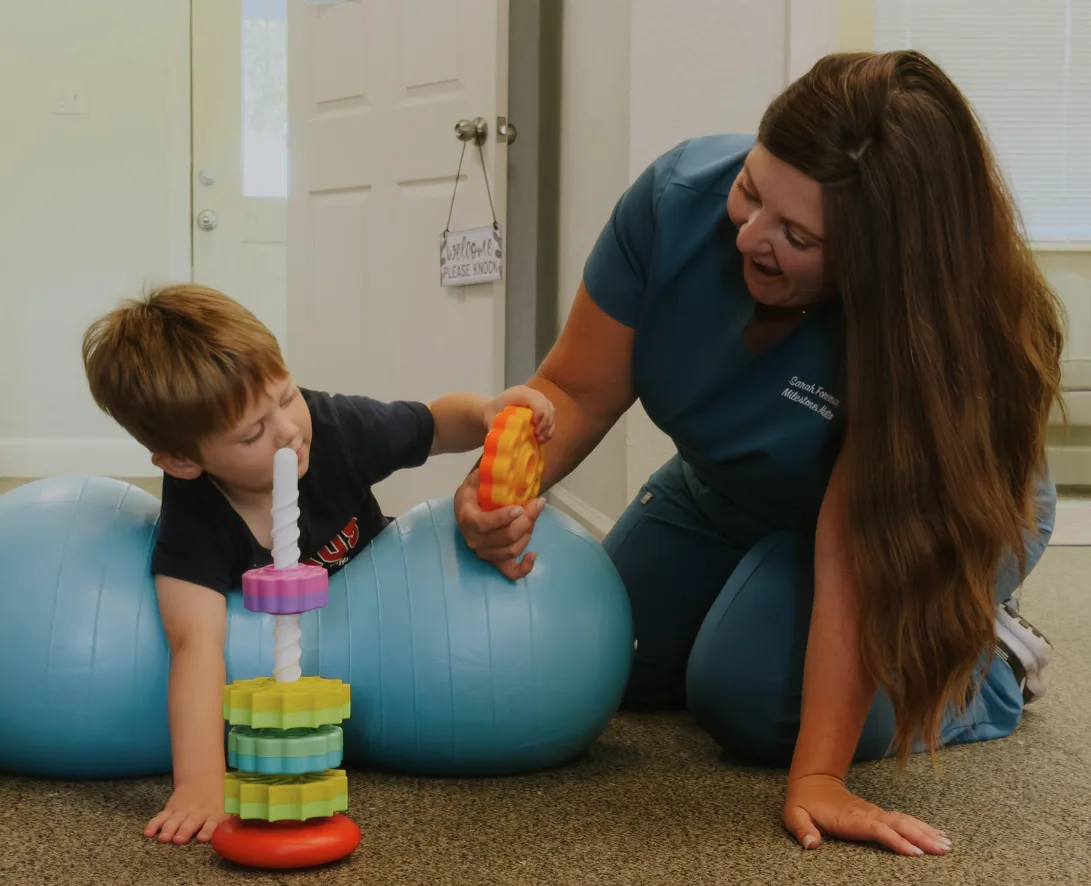 Pediatric therapist engaging a young child in play-based therapy with stacking rings and a sensory ball