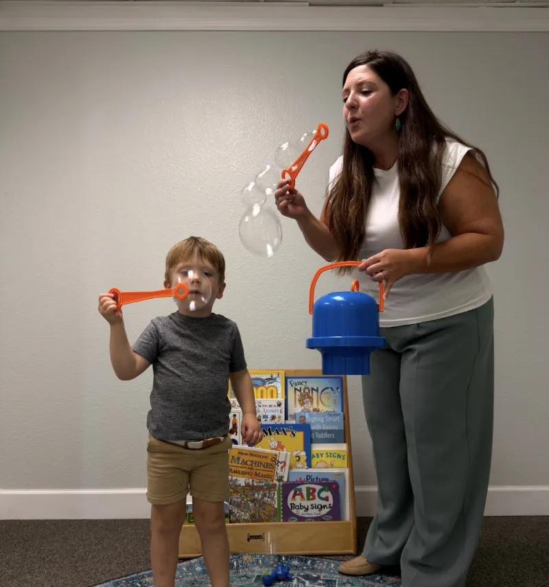 Speech therapist and young boy blowing bubbles together during a therapy session