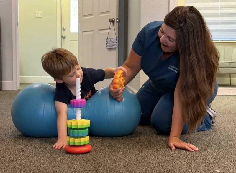 Therapist and young boy having fun stacking rings while balancing on exercise balls
