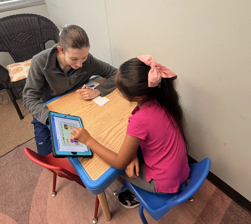 Therapist working with a young girl using an iPad during a speech therapy session